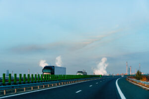 Trucks On Highway By Factory With Steam Against Morning Sky During Autumn